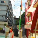 People salute a tall flagpole with the indian tricolor during a festive outdoor ceremony colorful bunting fluttering overhead Sarathi school habsiguda hyderabad