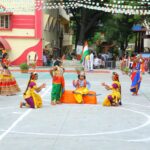 Group of girls in vibrant traditional indian costumes perform a dance on an outdoor courtyard festive bunting overhead and spectators in the background Sarathi school habsiguda hyderabad