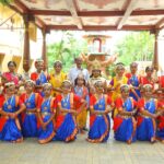 Group of young indian classical dancers in bright blue and red costumes with jewelry posing in two rows under a decorative pavilion with a man standing in the back sarathi school habsiguda hyderabad