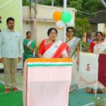 A woman in a red and white sari speaks at a podium decorated with orange white and green trim during a public event with balloons in indian flag colors behind her about to speak to an audience Sarathi school habsiguda hyderabad