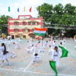 Schoolyard celebration with children in white uniforms performing dance as indian flag waves amid colorful bunting and confetti on the ground Sarathi school habsiguda hyderabad