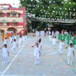 School children in white orange and green uniforms perform a ceremonial salute during a school parade on a decorated courtyard Sarathi school habsiguda hyderabad