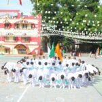 Group of students in white uniforms forming a circle with flags during a school parade on a sunny courtyard Colorful bunting overhead and a red yellow building in the background Sarathi school habsiguda hyderabad