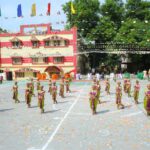 Group of young girls in green and purple traditional outfits performing a dance in a school courtyard with colorful flags overhead and spectators in the background Sarathi school habsiguda hyderabad
