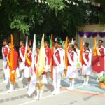 Group of students in red and white uniforms standing in a parade formation with colorful flags in a schoolyard  sarathi school habsiguda hyderabad