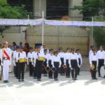 School marching band in white shirts and black pants performs with drums and cymbals on a parade ground spectators visible in the background under a canopy Sarathi school habsiguda hyderabad