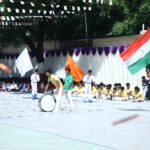 Children performing a flag parade with colored flags on a school stage indian flag visible in foreground Sarathi school habsiguda hyderabad