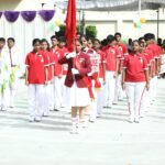 Students in a parade march in red polo shirts and white pants led by a flag bearer holding a red banner Sarathi school habsiguda hyderabad