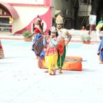 Children in colorful traditional indian dance costumes perform outdoors with a painted backdrop and onlookers in the background Sarathi school habsiguda hyderabad