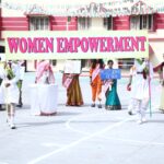 Group of schoolgirls and women standing in a courtyard under a large pink and green banner reading women empowerment holding colorful placards and props for an event that promotes gender equality Sarathi school habsiguda hyderabad