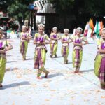 Group of young female dancers in lime and purple traditional costumes performing a synchronized dance outdoors with colorful flags in the background and confetti on the ground Sarathi school habsiguda hyderabad