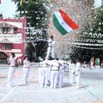 Students in white uniforms perform a flag raising ceremony as the indian tricolor is raised amid orange confetti in a school courtyard with festive banners Sarathi school habsiguda hyderabad