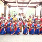 Group of bharatanatyam dancers in colorful blue and red sarees with jewelry posing with a man in white under a decorated pavilion in a temple courtyard Sarathi school habsiguda hyderabad