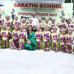 Group of young girls in purplegreen bharatanatyam costumes posing for a school independence day photo with a teacher in a green sari in front and a banner behind them Sarathi school habsiguda hyderabad